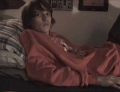 a man laying on top of a bed covered in a red sweatshirt and plaid pillow