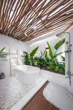 a white bath tub sitting under a bamboo roof in a bathroom next to a plant filled wall