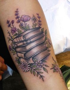 a woman's arm with a tattoo on it that has books and flowers around it