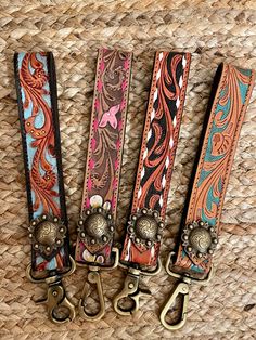 three different colored belts with metal handles on a woven cloth background, one has an antique style buckle and the other is decorated with flowers