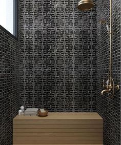 a bathroom with black and white tiles on the wall, shower head, and wooden bench