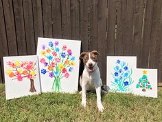 a dog is sitting in the grass next to three canvass with flowers painted on them