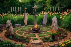 a fire pit in the middle of a garden surrounded by rocks and grass with flowers around it