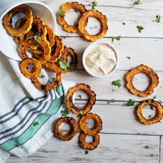 some onion rings are on a plate with dip and cilantro leaves next to them