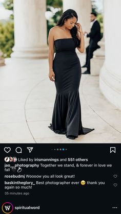 a woman in a long black dress standing on the sidewalk talking on her cell phone