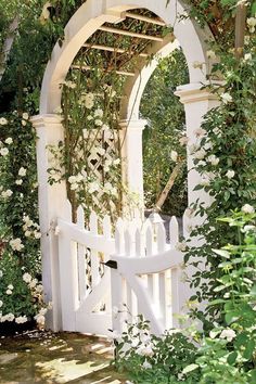 a white gate surrounded by flowers and greenery