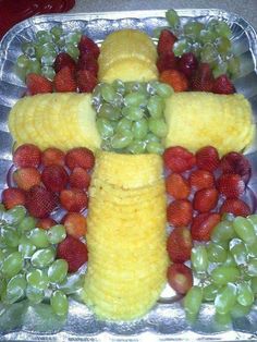 a cross made out of fruit on top of a metal pan filled with grapes, strawberries and pineapples