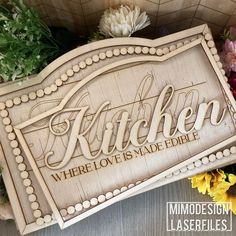 a wooden sign that says kitchen where love is made edible with flowers in the background