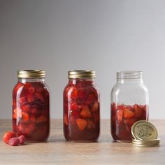 three jars filled with pickled fruit sitting on top of a wooden table next to a coin