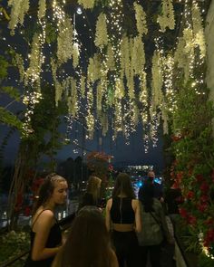 people are walking down a walkway with lights hanging from the ceiling and flowers all around