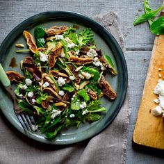 a green salad with nuts and feta cheese on a plate next to a cutting board