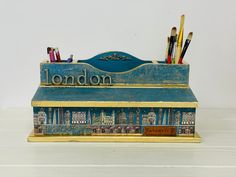 a pen holder with pencils and markers in it on a white table next to a wall