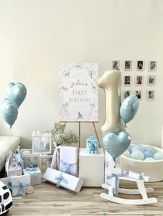 a first birthday party with blue balloons and gifts on the floor in front of a sign