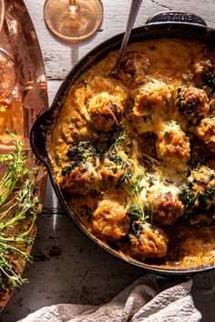 a casserole dish with meat and vegetables in it on a wooden table next to wine glasses