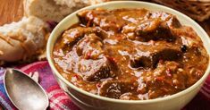 a bowl of beef stew with bread on the side