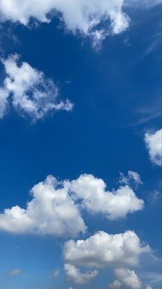 an airplane is flying high in the blue sky with white fluffy clouds and some green grass