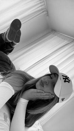 black and white photograph of a woman laying on her stomach wearing a baseball cap, jeans and sneakers