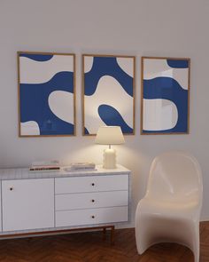 two blue and white paintings hang on the wall next to a dresser with a lamp