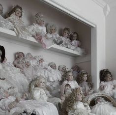 a group of dolls sitting on top of shelves next to each other in white dresses