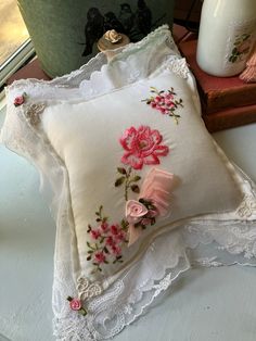 two decorative pillows with pink flowers on them sitting on a table next to a vase