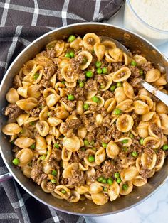 a skillet filled with pasta and peas next to a glass of milk