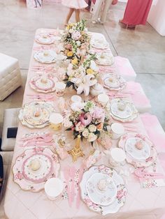 a long table with pink and white plates, flowers and napkins on it is set up for a tea party