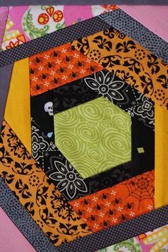 a close up of a patchwork quilt on a pink surface with an orange and black hexagon