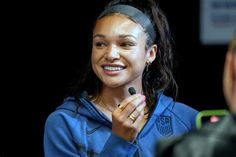 a young woman smiles as she talks to another person in front of her onlooker