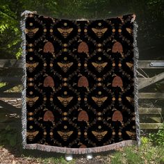 a black and gold blanket with an image of two bees on it, in front of a wooden fence