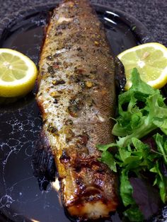 a plate with fish, greens and lemons on it