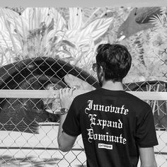 a man standing in front of a fence looking at an animal behind him with his hand on his chin