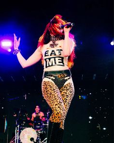 a woman with red hair and leopard print pants on stage holding a microphone in her hand