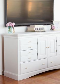 a flat screen tv mounted on top of a white dresser