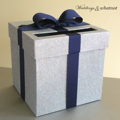 a silver gift box with a blue ribbon on it's side, sitting on a table