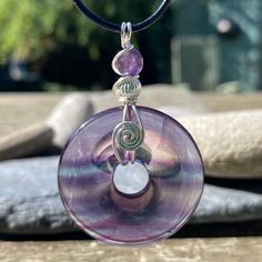 Top quality AA Fluorite gemstone donut shaped Healing stone on a black necklace cord. A gemstone purple and sometimes green crystal pendant on black adjustable length cord. Vegan cord approx 30" adjusts to 15" This is a lovely green and purple striped gemstone made from natural flourite. I have added my Sterling Silver bead to make the design individual. This has a tie closure with double knots that slide to adjust the length. The solid silver bead is optional FLOURITE: aid to reduce stress and Fluorite Gemstone, Donut Pendant, Gemstone Drop Earrings, Boho Crystal, Donut Shape, Necklace Cord, Healing Necklace, Green Crystal, Purple And Green