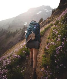 a woman with a backpack walking up a trail in the mountains on a sunny day