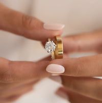 two hands holding wedding rings with one hand on the other's finger, both wearing gold and white