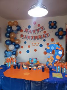 a birthday party set up with blue and orange balloons, paper streamers, and cupcakes