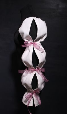 three pieces of white cloth tied together with pink ribbon and bows on black mannequins