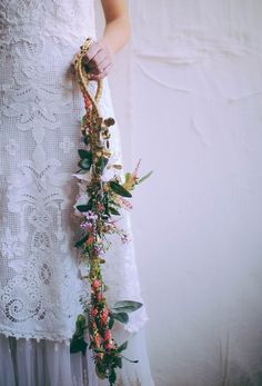 a woman in a white dress holding a flower lei attached to her waist with leaves and flowers on it