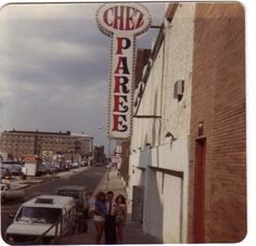 people are standing on the sidewalk in front of a building with a sign that says cheez pareree