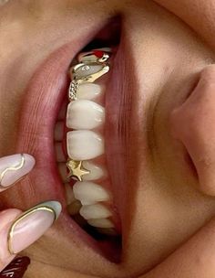 a woman's mouth with gold and white decorations on her teeth, while holding onto a ring