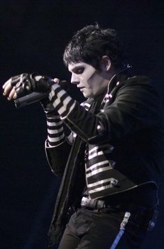 a male in a black and white striped jacket holding a microphone with his right hand