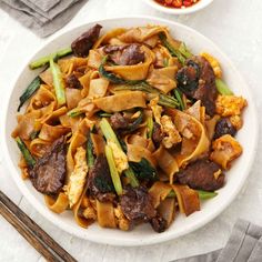 a white bowl filled with noodles and meat on top of a table next to chopsticks