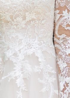 the back of a wedding dress with white lace on it and flowers in its bouquet