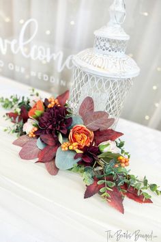 a wedding cake decorated with flowers and leaves on top of a white table cloth covered box