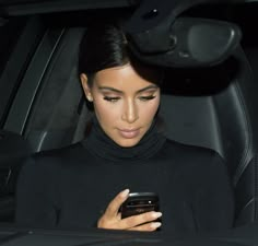 a woman sitting in a car looking at her cell phone