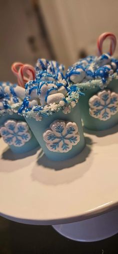 some candy canes are in small blue cups on a white plate with snowflakes and candy canes