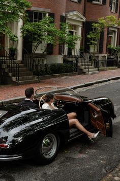 a man and woman are sitting in an old fashioned car on the side of the road