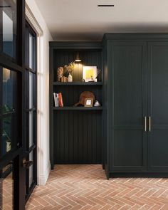 a black bookcase in the corner of a room with wooden floors and dark green cabinets